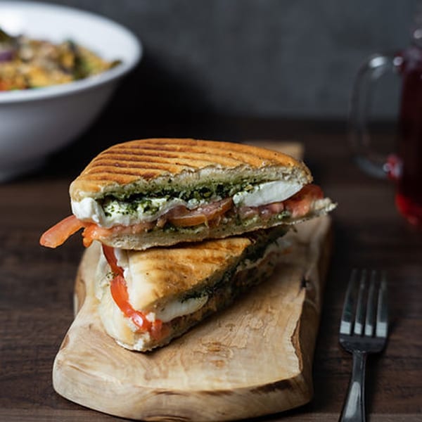 Grilled panini sandwich with pesto, mozzarella, and tomato on a wooden board.