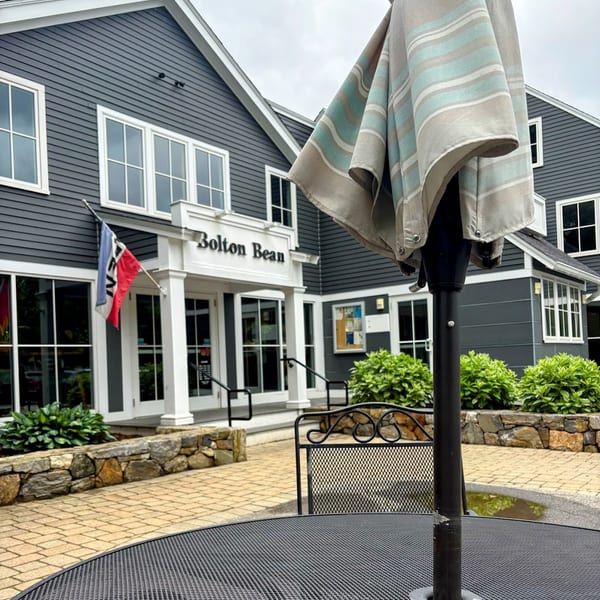 Outdoor patio table with umbrella, overlooking the Bolton Bean coffee shop entrance on a cloudy day.